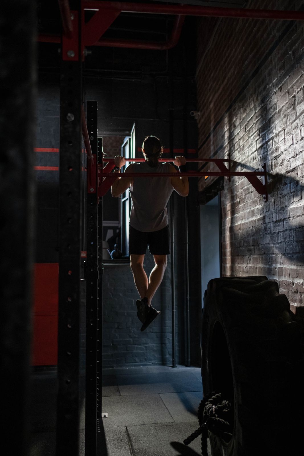 A man seen from behind doing a pull-up in a dark gym